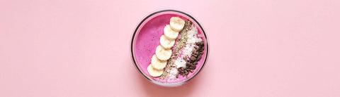 Smoothie bowl – muz dilimleri, kakao parçaları, hindistan cevizi ve tohumlarla süslenmiş pembe kahvaltı kasesi