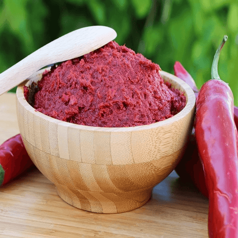 Tatlı Biber Salçası-1000 Gr. ahşap kasede taze biber salçası, yanında kırmızı biberler.